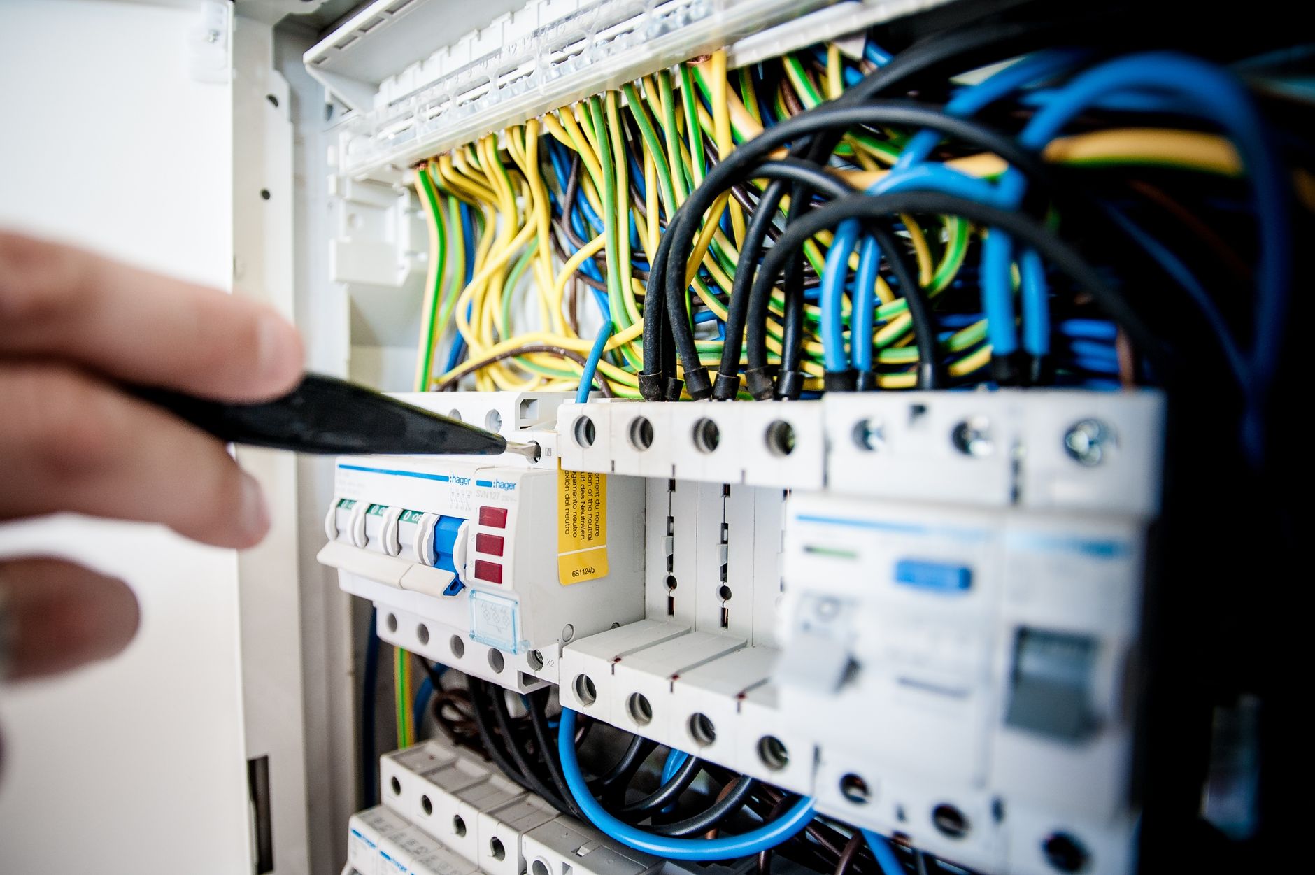 An electrician working inside an opened switchboard, the kind of service call a CRM for electricians in Bradford is built to capture