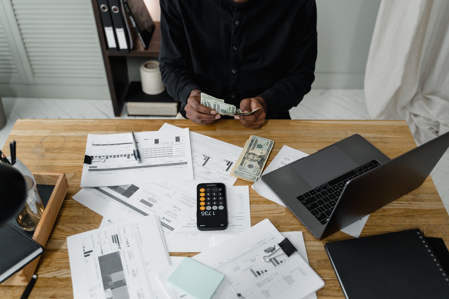 A person counting dollar bills at a desk while allocating a marketing budget across channels