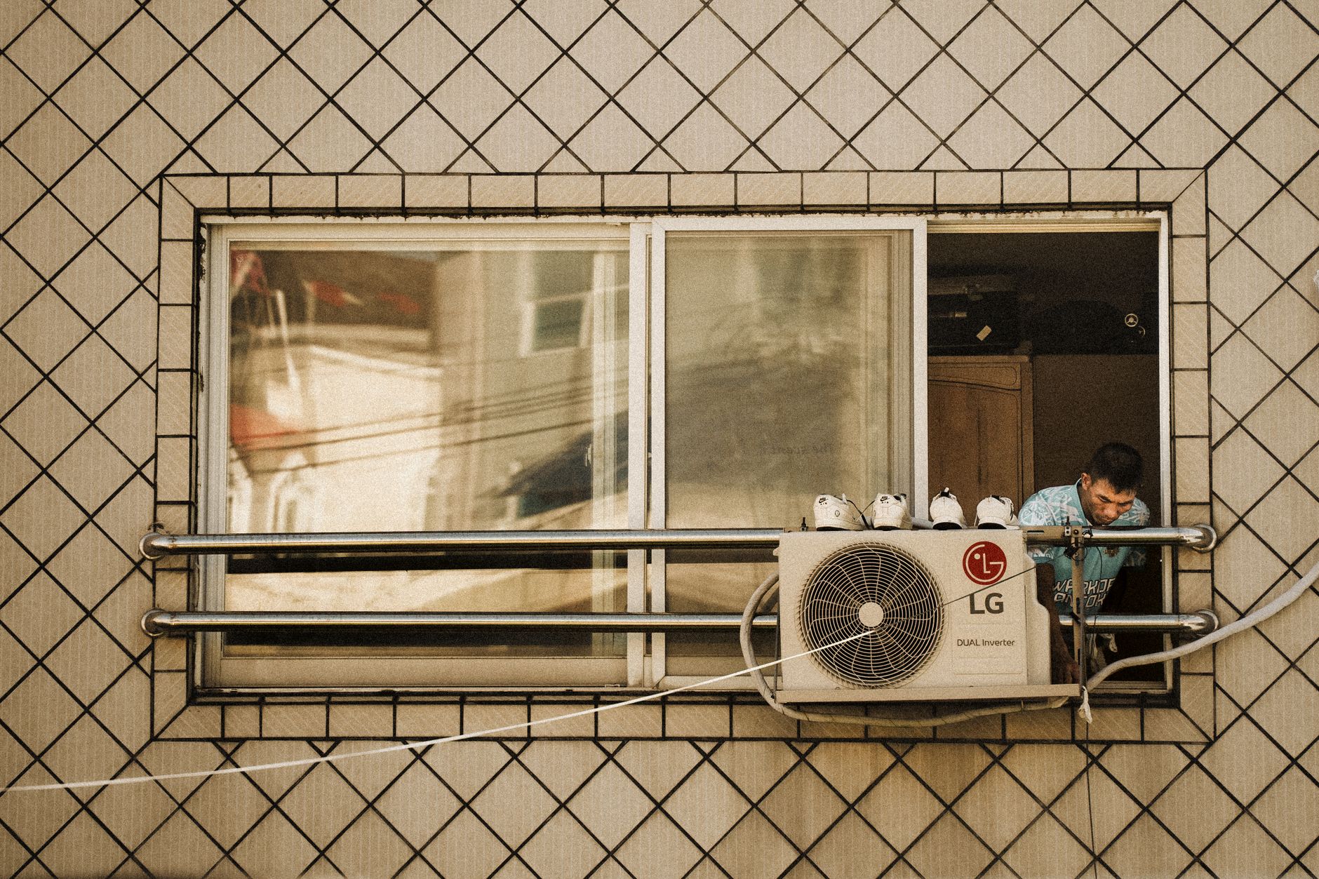 A technician working beside an outdoor air conditioning unit mounted under a window