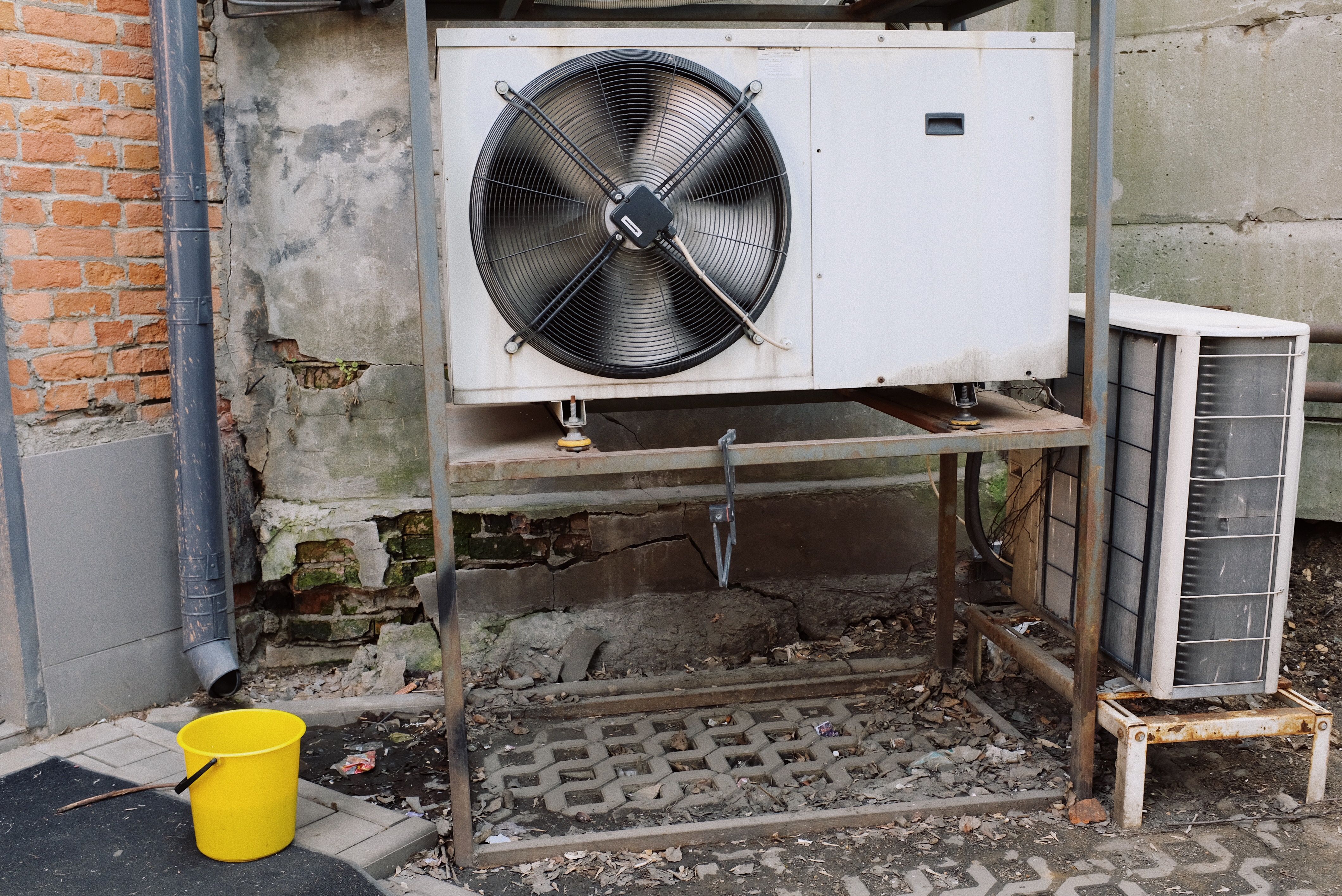 An outdoor air conditioning condenser unit mounted against an exterior wall