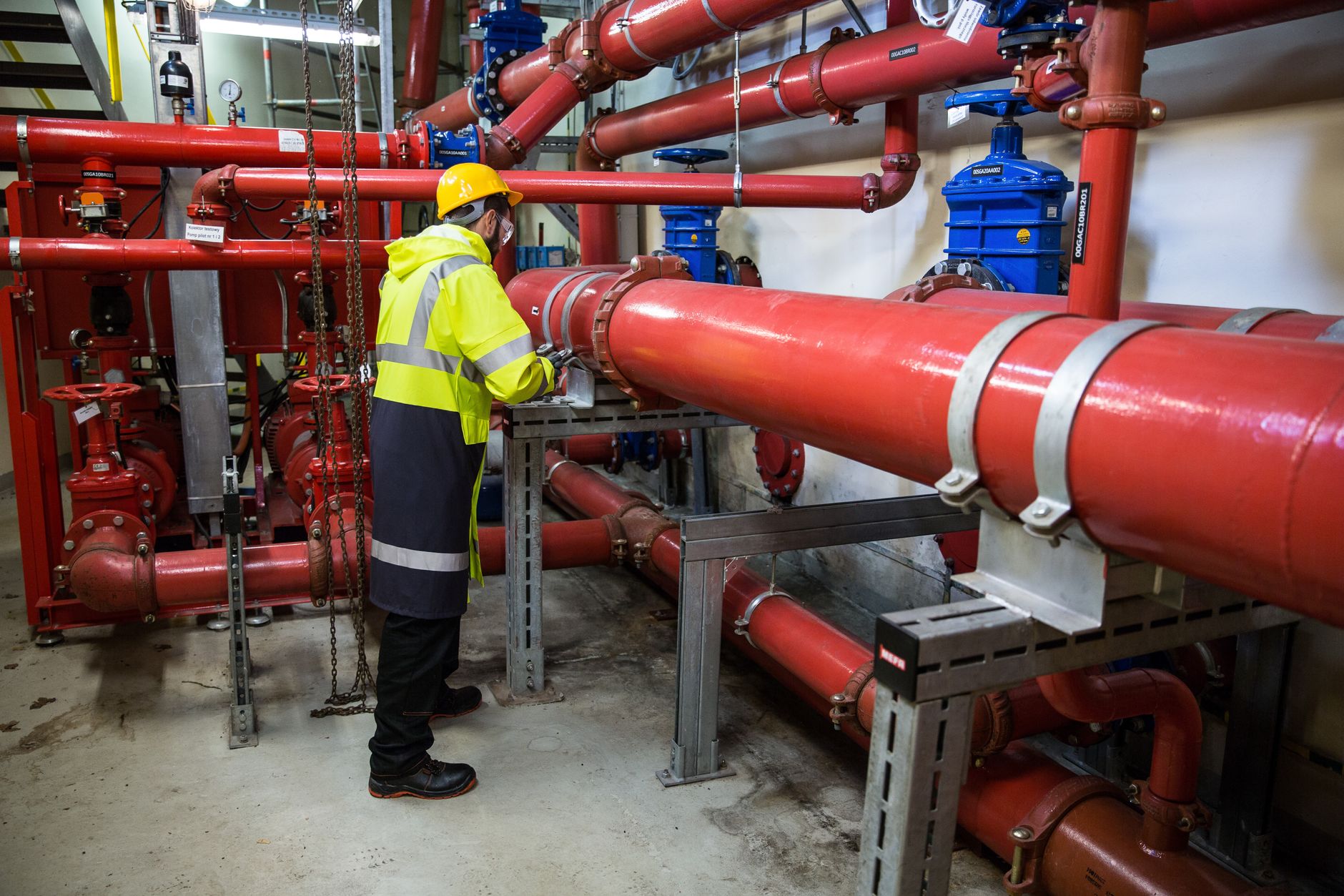 A technician in hi-vis gear tightening a fitting on large red water pipes, local SEO for plumbers in Sudbury starts with being the shop people call