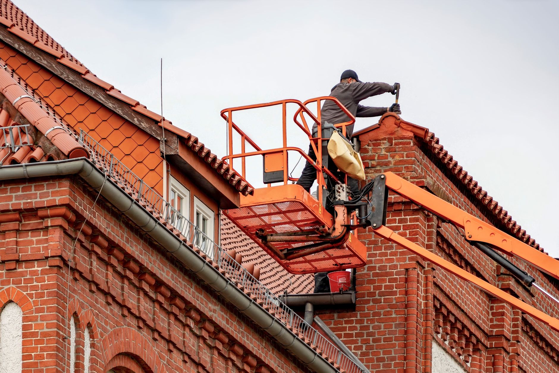 A roofer working from an aerial lift platform repairing tile roofing on a brick building, the kind of on-the-job work local SEO for roofers in Alliston is meant to bring more calls for