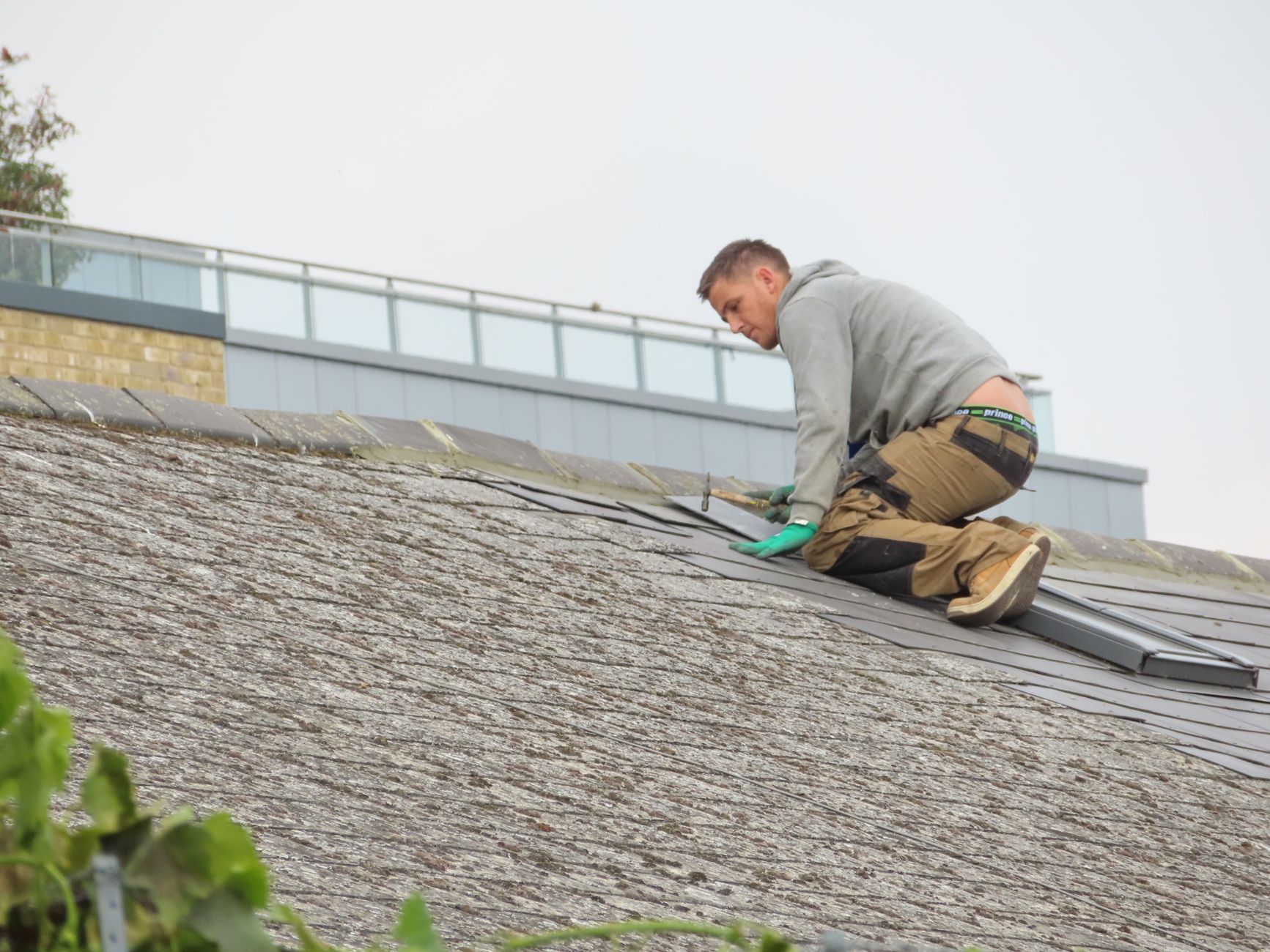 A roofer installing individual shingles by hand on a house roof