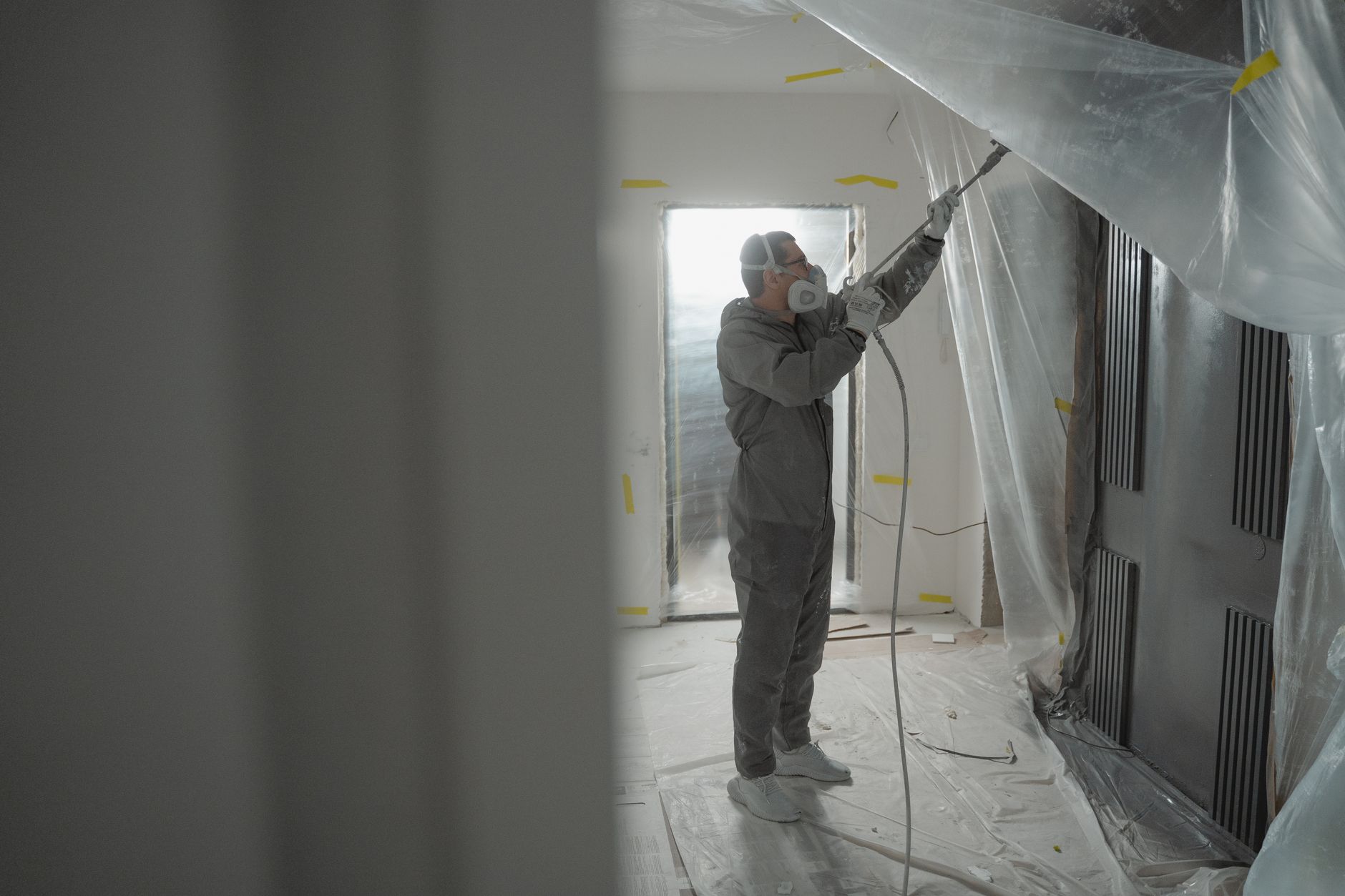 Contractor in coveralls and a respirator spray-painting an interior behind plastic sheeting, the kind of job-site moment worth filming for contractor video marketing