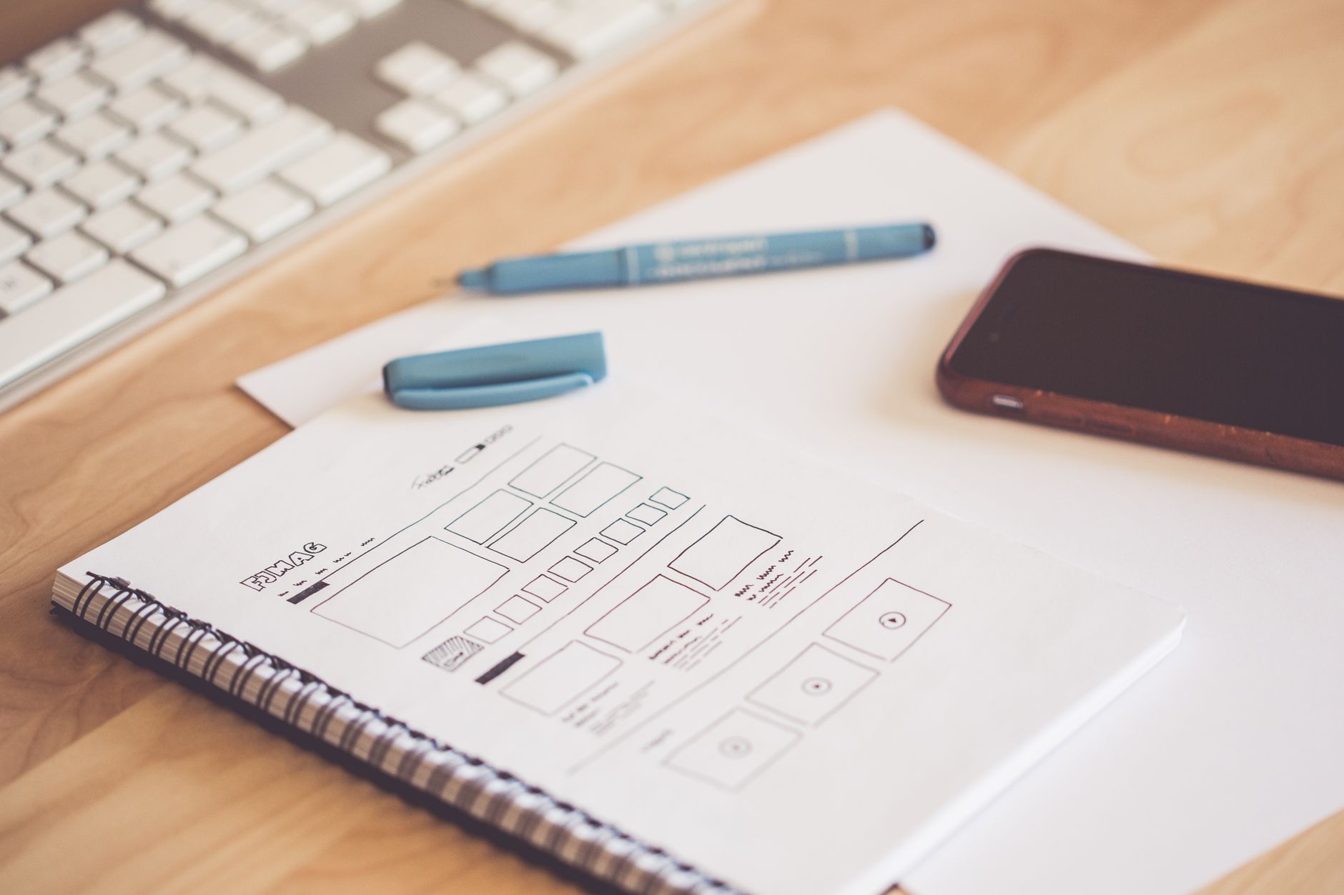 A website wireframe sketched in a spiral notebook beside a pen, keyboard and phone, the kind of page plan that helps a site rank